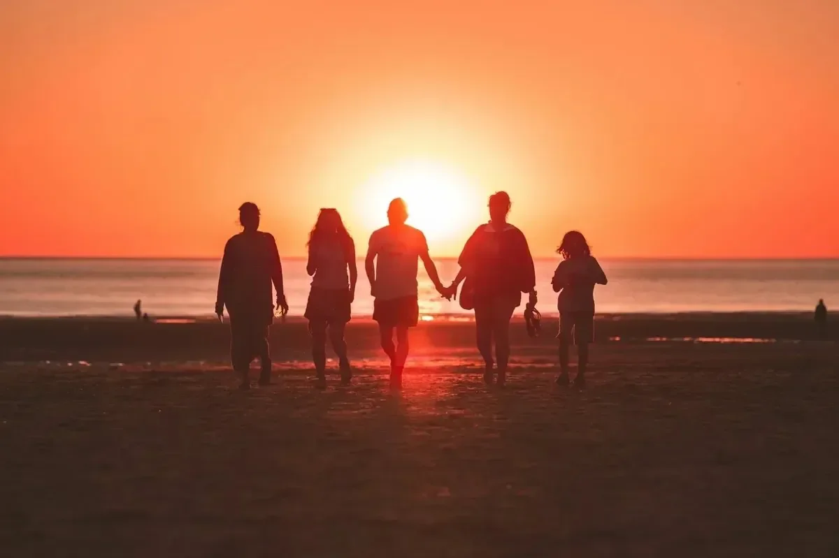 A family silhouetted walking hand in hand toward the ocean at sunset
